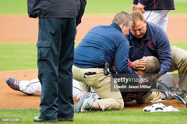 Starting pitcher Carlos Carrasco of the Cleveland Indians is helped up by team trainers after being hit in the face by a line drive off the bat of...
