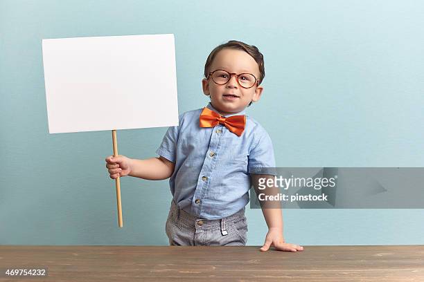 nerdy child holding a blank sign in a classroom - placard stockfoto's en -beelden
