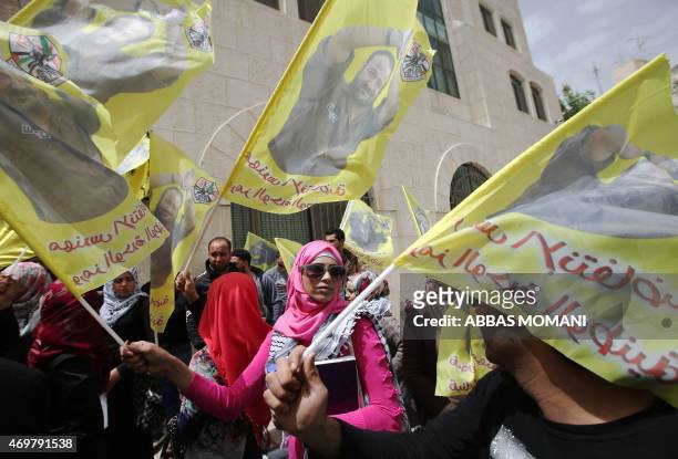 Palestinian protesters wave flags bearing portraits of Fatah leader Marwan Barghuti, jailed in Israel, during a march to mark the anniversary of his...