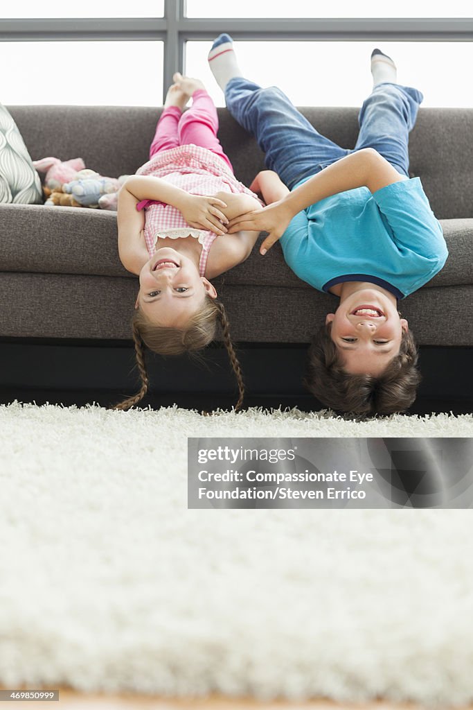 Brother and sister hanging upside down on sofa