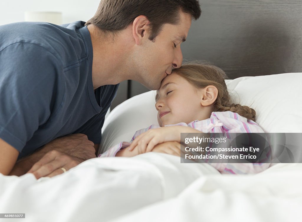 Father kissing daughter on forehead in bedroom