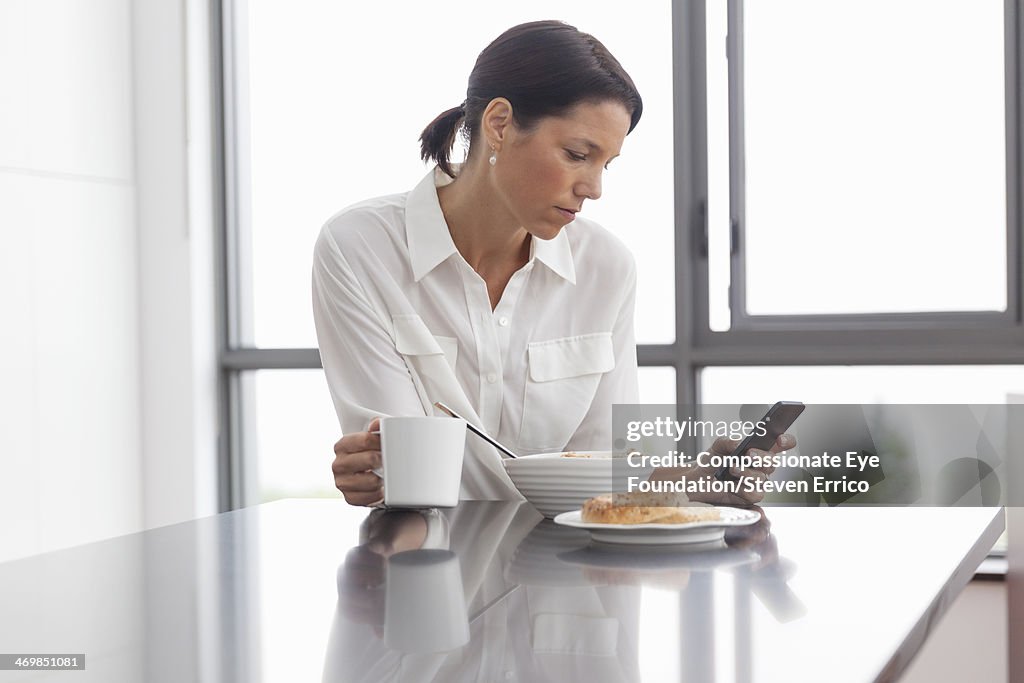 Woman having breakfast using mobile phone
