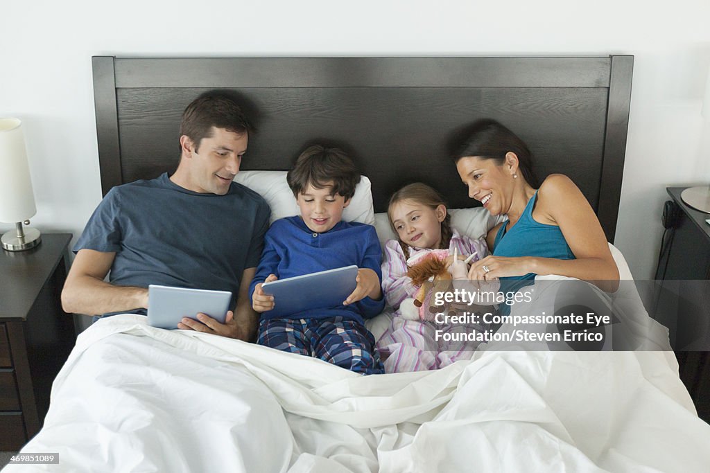 Family in bed using digital tablets