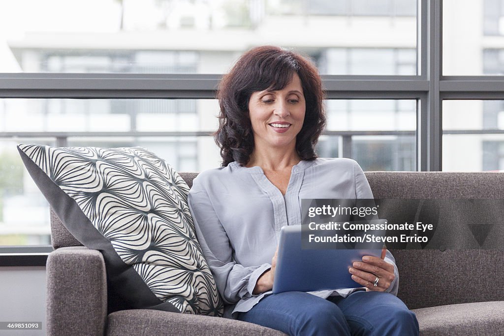 Mature woman on sofa using digital tablet