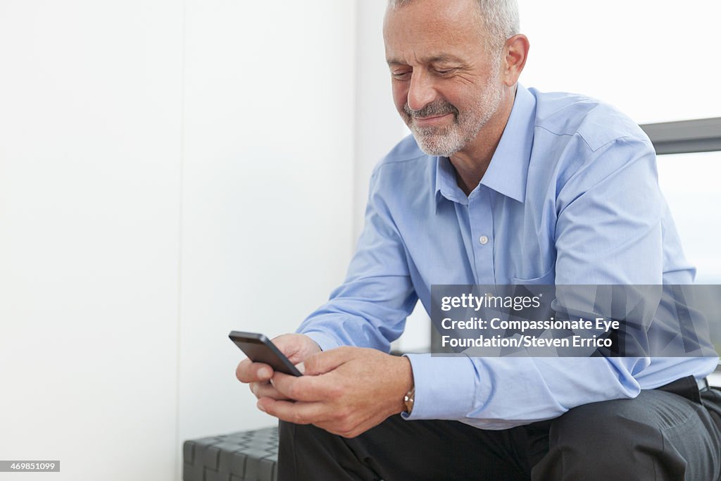 Mature man by window texting on mobile phone