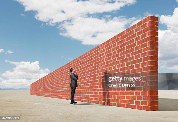 businessman looking up at brick wall in middle of desert - barricade stockfoto's en -beelden