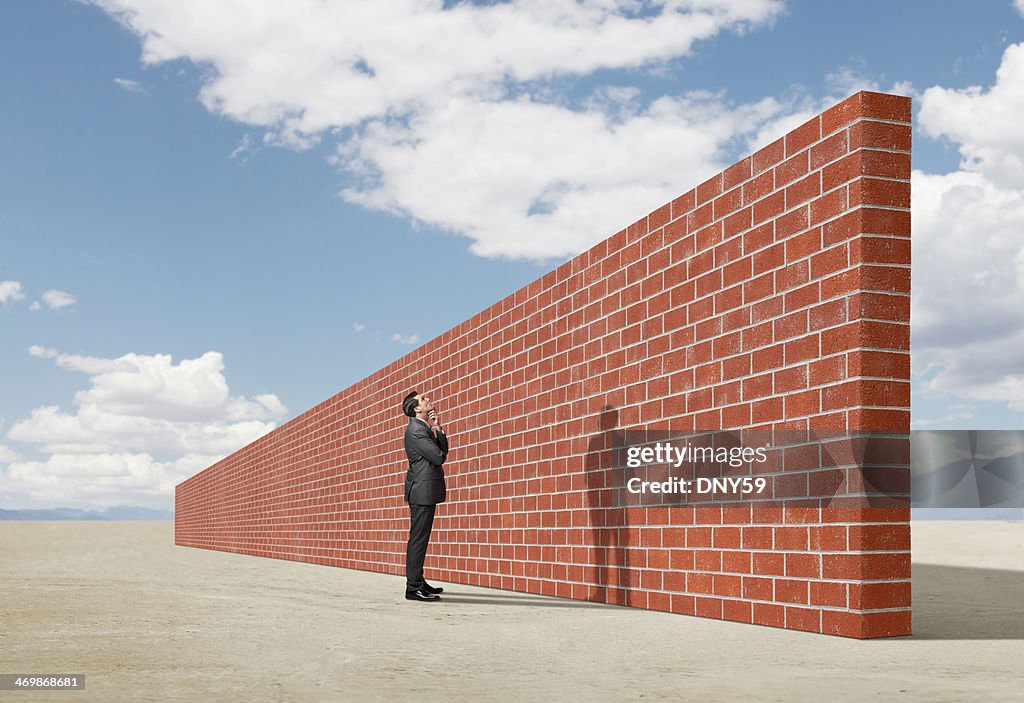 Businessman looking up at brick wall in middle of desert