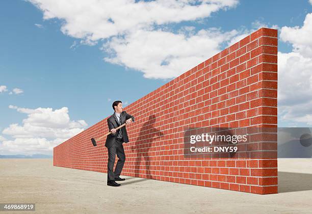 businessman trying to break down barrier created by brick wall - swinging sledgehammer stock pictures, royalty-free photos & images