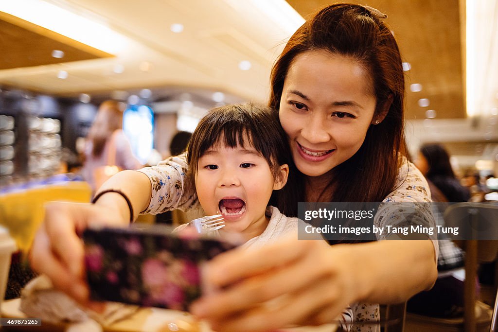 Mom & toddler girl taking selfie joyfully in cafe