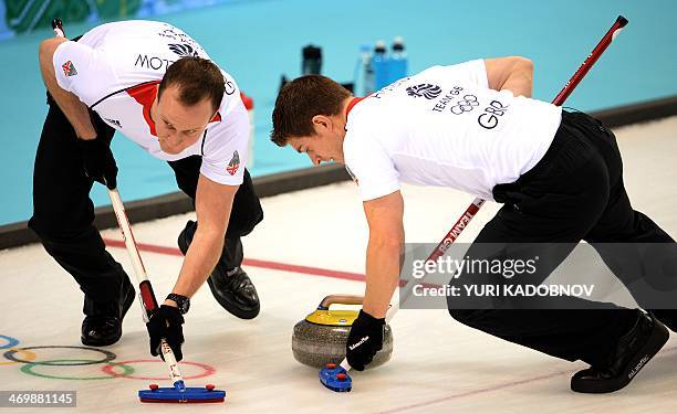 Great Britain's Michael Goodfellow and Scott Andrews clean the way for the stone during the 2014 Sochi Winter Olympics Men's Curling Round Robin...