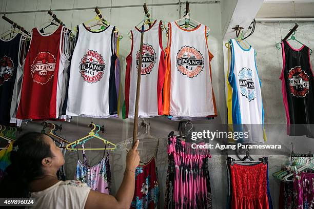 Woman puts a Bali Bintang beer singlet shirt on the shelf of her shop at Popies Lane II Street on April 16, 2015 in Kuta, Bali, Indonesia. Indonesia,...