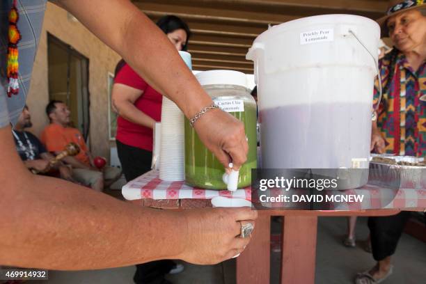 Man draws a cup of cactus and chia lemonade, next to a container of prickly pear cactus lemonade, as people are served Native dishes at the annual...