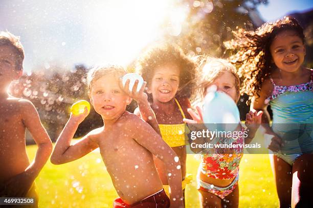 mezclada raza grupo de niños tirando water balloons at camera - water garden fotografías e imágenes de stock