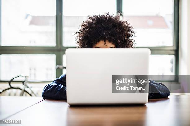 mujer joven trabajando en espacio de tipo loft detrás de una computadora portátil - working behind laptop fotografías e imágenes de stock