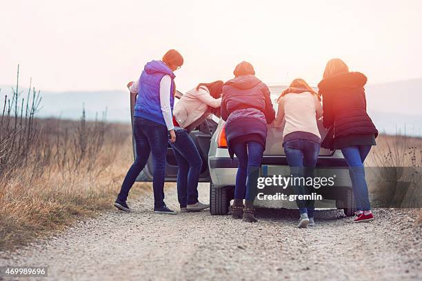 group of friends pushing car on the rural road - broken friendship stock pictures, royalty-free photos & images