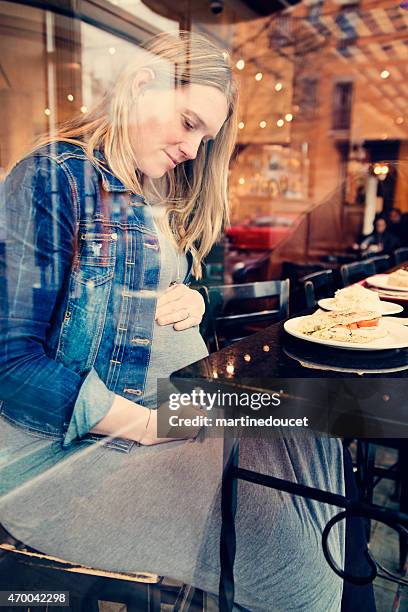 Pregnant woman eating alone at a restaurant holding belly.