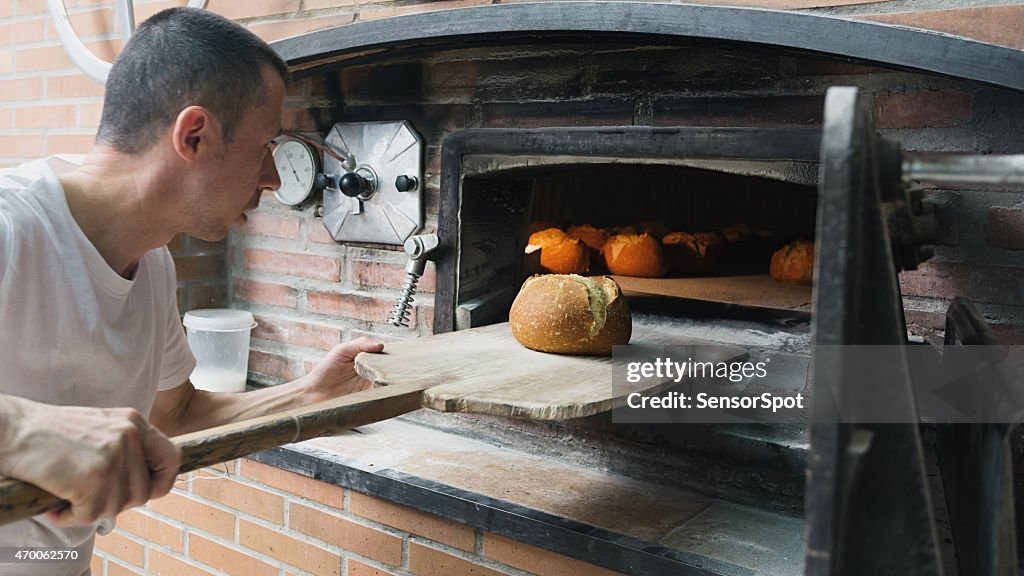 Baker checking a bread loaf in a traditional stove.