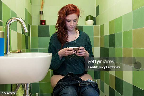 young woman checking social media on the toilet - woman in bathroom stockfoto's en -beelden