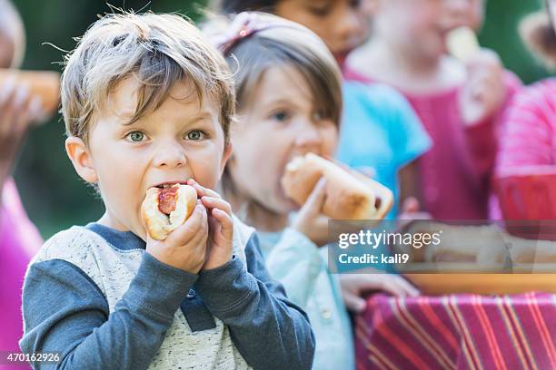 little boy eating a hotdog at a cookout - hotdog stockfoto's en -beelden