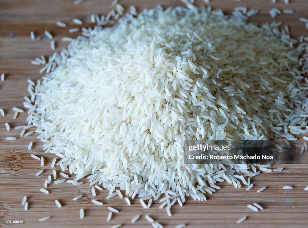 Small pile of long grain white rice over a wooden surface...