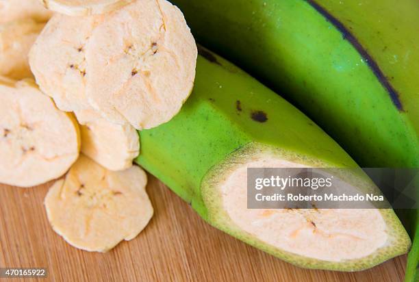 Cuban Cuisine: Delicious green plantain bananas over wood cutting board along with chips or fries and a fruit with a transversal cut.