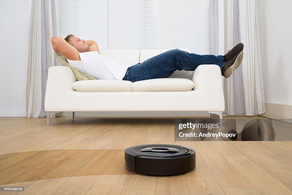 Robotergestützte Staubsauger vor Mann entspannend
