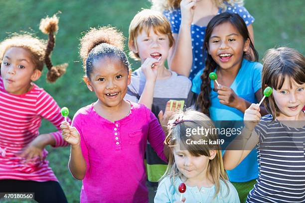 group of multiracial children eating lollipops - lolly stockfoto's en -beelden