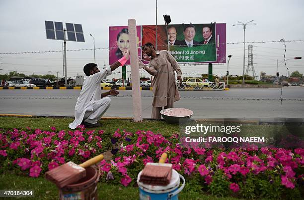 Pakistani labourers decorate the roadside in front of a welcoming billboard featuring pictures of visiting Chinese President Xi Jinping and his...