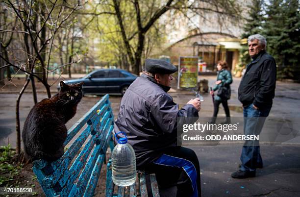 Cat is perched on a bench as a man collecting water takes a cigarette break in Donetsk on April 18, 2015 in the self-proclaimed Donetsk People's...