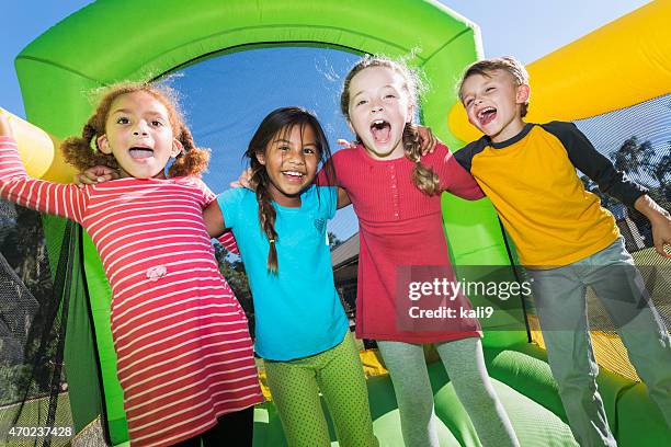 vier multi-ethnischen kinder spielen auf hüpfburg - inflatable playground stock-fotos und bilder