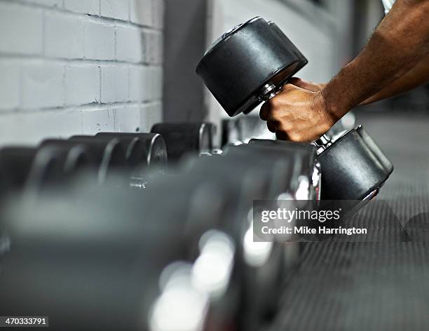 athletic male picking up dumbbells in gym - mancuerna fotografías e imágenes de stock