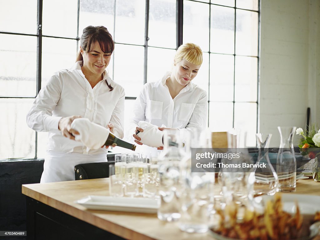 Smiling waitresses standing pouring Prosecco