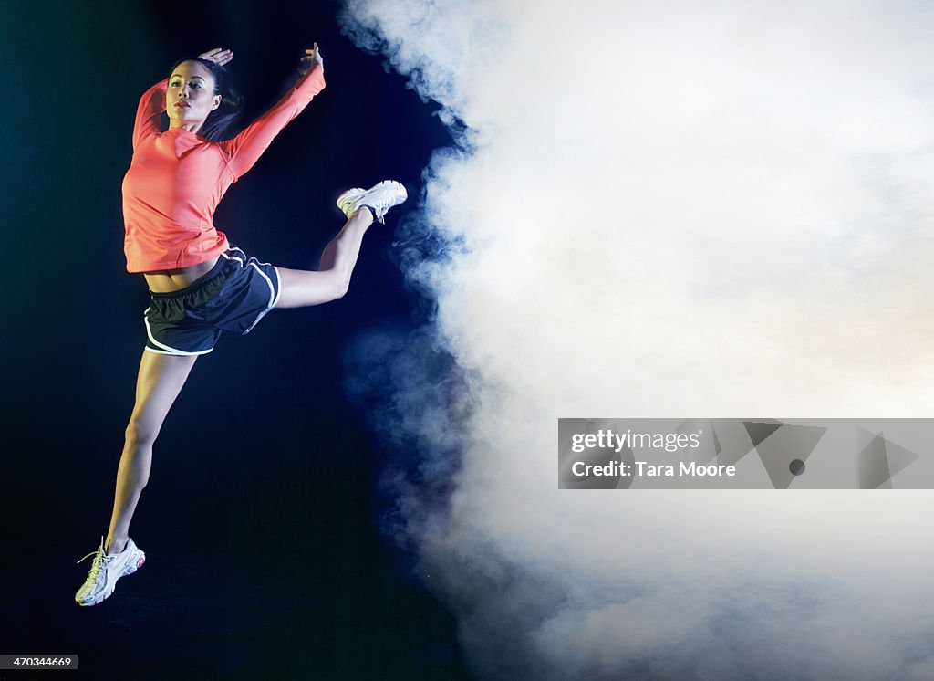 Sports woman jumping through smoke