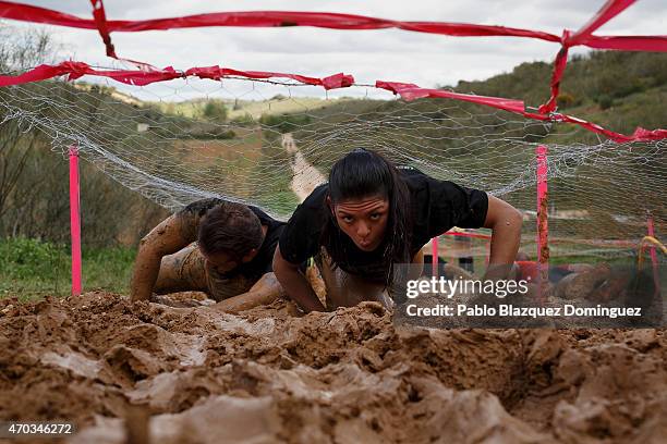 Competitors climb a muddy bank under a wire fence during the first Belik Race on April 19, 2015 in Cabanillas del Campo, in the region of...