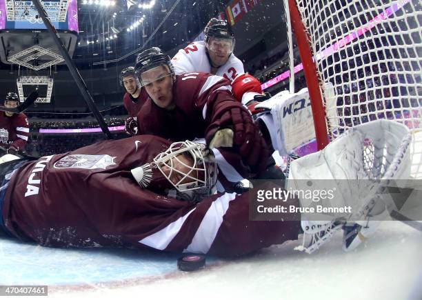 Kristers Gudlevskis of Latvia makes a save against Canada during the third period with the help of teammate Kristaps Sotnieks during the Men's Ice...