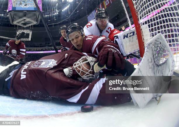 Kristers Gudlevskis of Latvia makes a save against Canada during the third period with the help of teammate Kristaps Sotnieks during the Men's Ice...