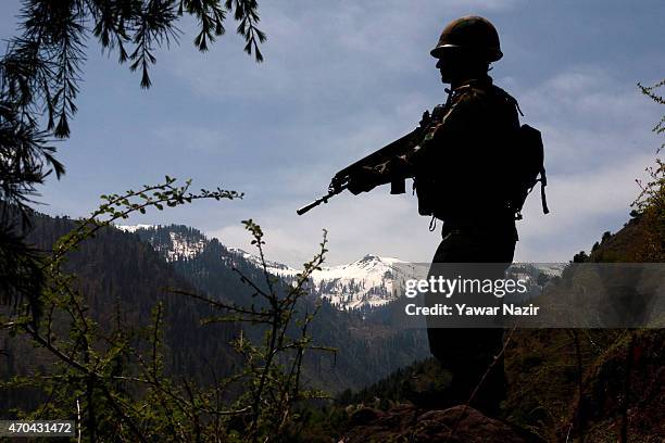 An Indian army soldier is silhouetted against the snow capped mountains of Pakistan administered Kashmir as he guards the the Line Of Control on...