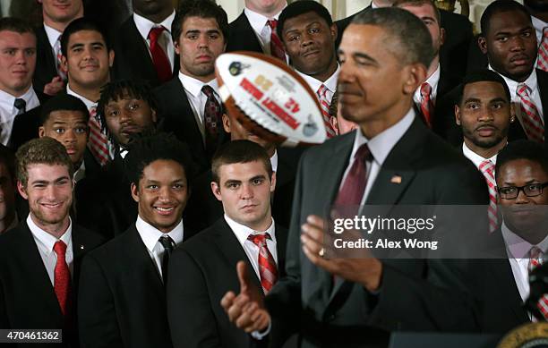 President Barack Obama plays with a football as members of the Ohio State University Buckyes football team look on during an East Room event at the...