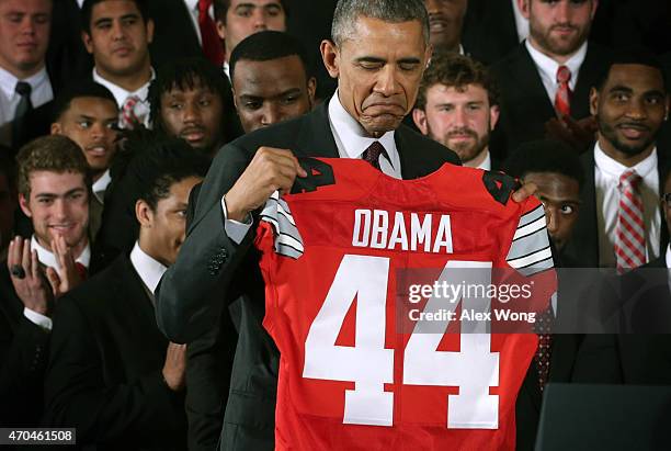 President Barack Obama receives a team jersey as he hosts the Ohio State University Buckyes football team during an East Room event at the White...