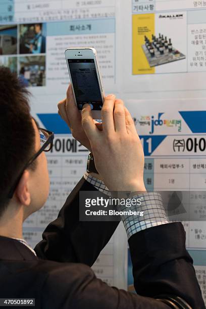 Jobseeker takes a photograph of job listings using his Apple Inc. IPhone 5 smartphone at a job fair in Goyang, South Korea, on Tuesday, April 21,...