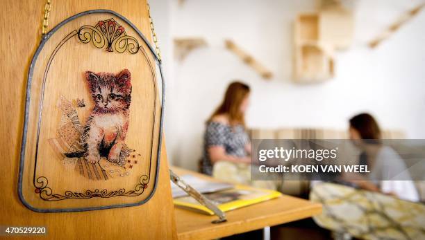 Two women sit in the first cat cafe in Amsterdam, the Netherlands, as a sign bearing a cat hung on a wall on April 21, 2015. Already popular in Tokyo...
