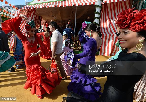 Women wearing the traditional flamenco dresses, often in bright colors, and accessorized with flower in hair dance around casetas at the 'Feria de...