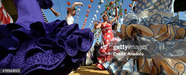 Women wearing the traditional flamenco dresses, often in bright colors, and accessorized with flower in hair dance around casetas at the 'Feria de...