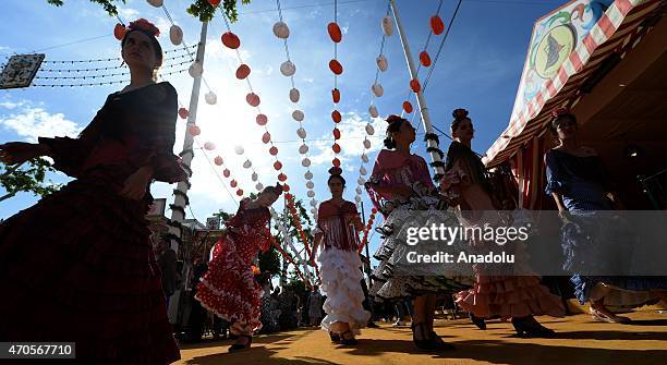 Women wearing the traditional flamenco dresses, often in bright colors, and accessorized with flower in hair dance around casetas at the 'Feria de...