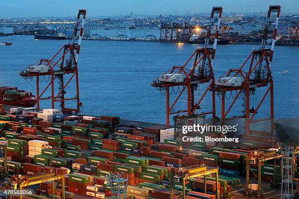 Shipping containers sit stacked next to gantry cranes on the dockside at a shipping terminal at dusk in Tokyo, Japan, on Tuesday, April 21, 2015....