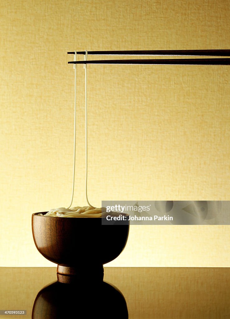 Noodle bowl with 2 chopsticks holding up 2 noodles
