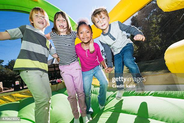 vier multi-ethnischen kinder spielen auf hüpfburg - bouncy castle stock-fotos und bilder