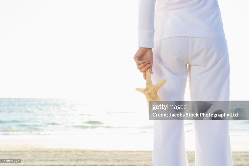 Hispanic woman holding starfish on beach