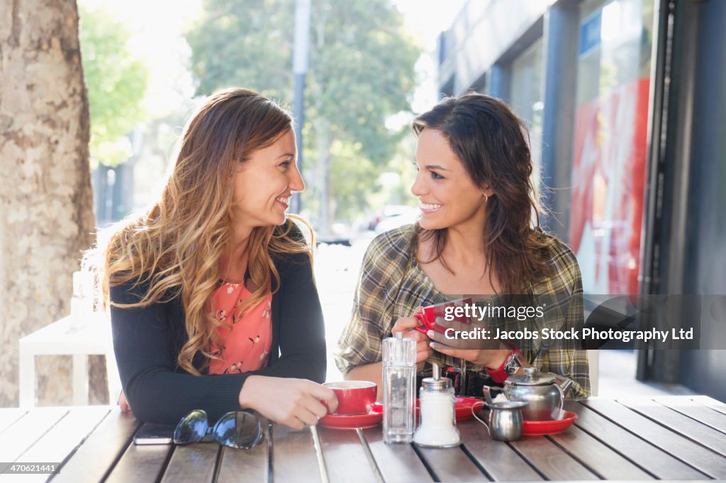 Mixed race women having tea at sidewalk cafe