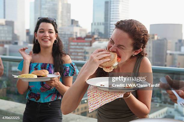 friends enjoying barbecue on urban rooftop - woman eating burger stockfoto's en -beelden